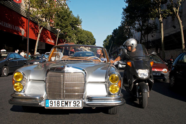 Vintage Mercedes and scooter driver exchange conversation at pedestrian crossing